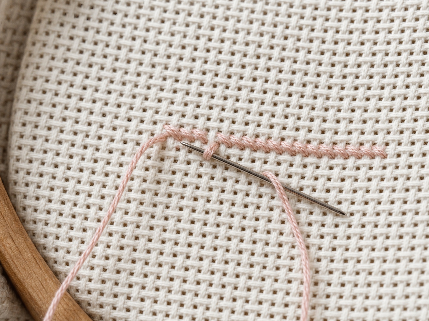 The back of Aida fabric showing a thread tail secured under stitches