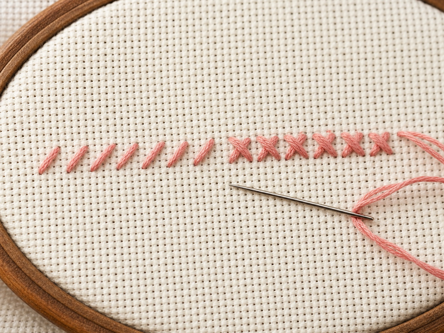 A row of half-stitches and completed cross stitches in pink thread